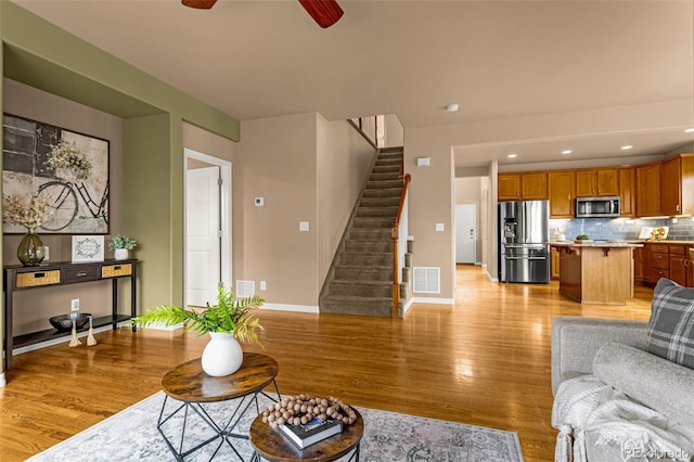 living area with light wood finished floors, visible vents, baseboards, stairway, and a ceiling fan