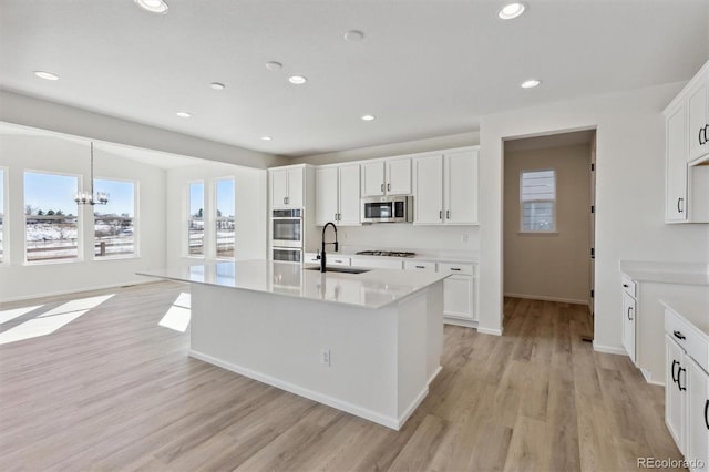 kitchen with light wood-type flooring, stainless steel appliances, a kitchen island with sink, a chandelier, and white cabinetry