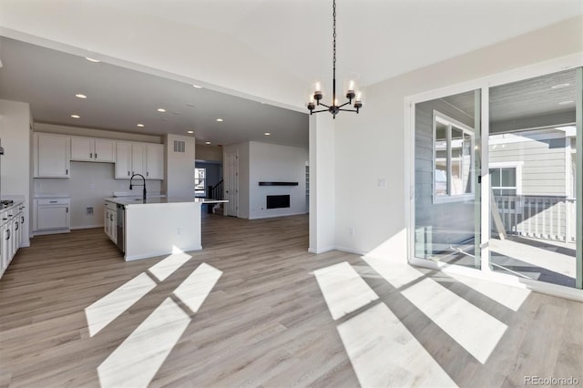 kitchen featuring light wood-type flooring, a kitchen island with sink, sink, decorative light fixtures, and white cabinetry