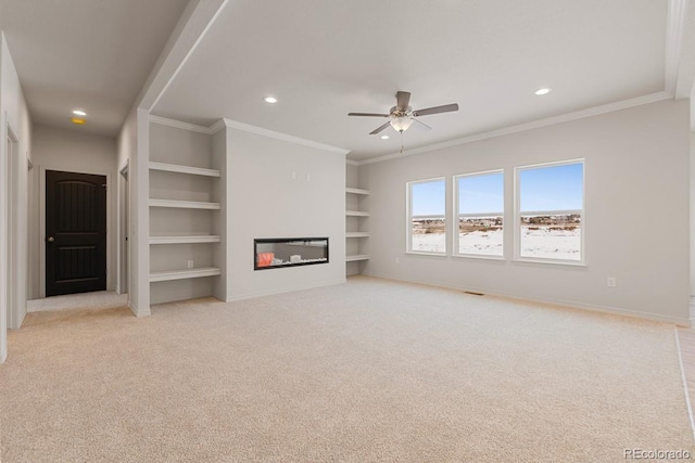 unfurnished living room featuring built in shelves, ceiling fan, ornamental molding, and light carpet