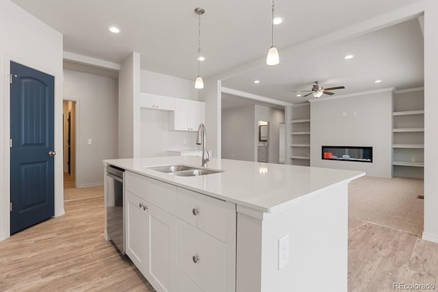 kitchen featuring white cabinetry, a kitchen island with sink, sink, and decorative light fixtures