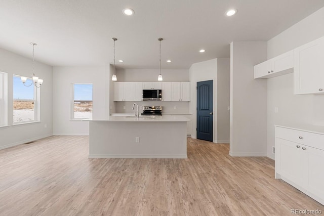 kitchen featuring white cabinetry, hanging light fixtures, a center island with sink, light hardwood / wood-style flooring, and stainless steel appliances