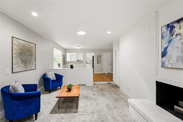 carpeted living room featuring a fireplace, recessed lighting, and brick wall