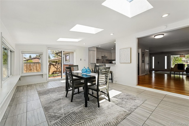 dining area with a skylight, light tile patterned floors, and baseboards