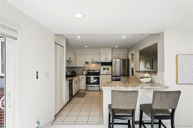 kitchen with appliances with stainless steel finishes, a peninsula, a breakfast bar, backsplash, and recessed lighting