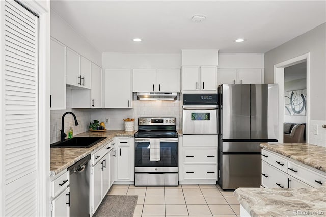 kitchen featuring stainless steel appliances, a sink, under cabinet range hood, light tile patterned floors, and white cabinetry