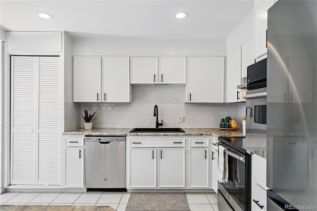 kitchen featuring stainless steel appliances, a sink, light tile patterned floors, white cabinets, and backsplash
