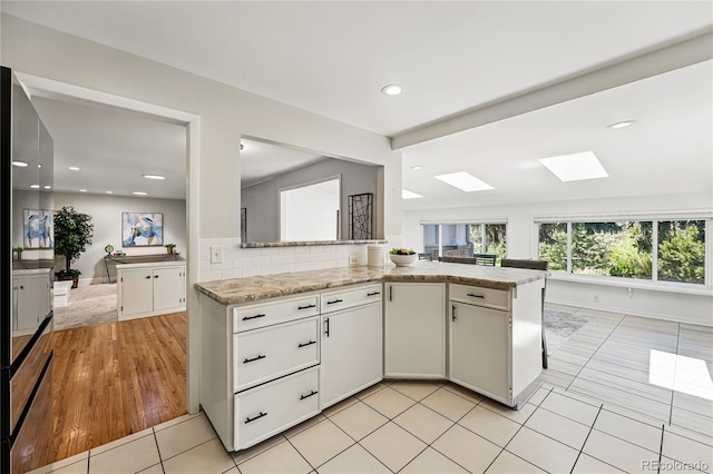 kitchen with a skylight, white cabinetry, light tile patterned floors, tasteful backsplash, and light stone counters
