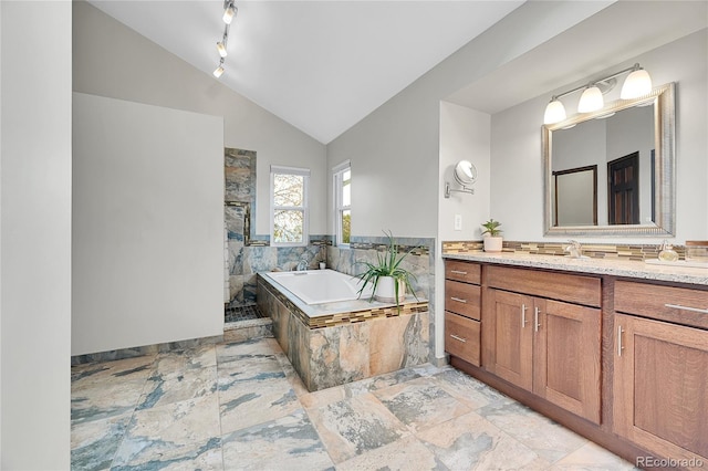 bathroom featuring stone finish flooring, a garden tub, lofted ceiling, a stall shower, and vanity