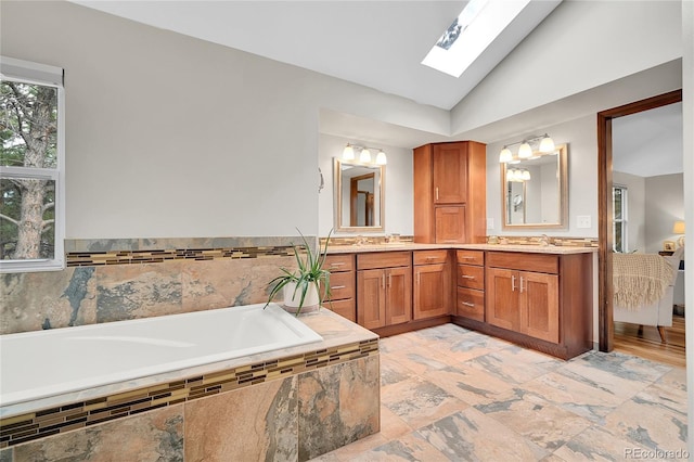 full bath featuring double vanity, vaulted ceiling with skylight, a bath, and a sink