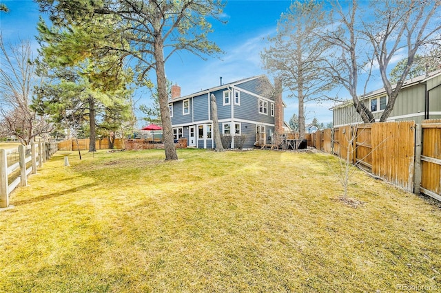 rear view of house with a fenced backyard, a chimney, and a yard