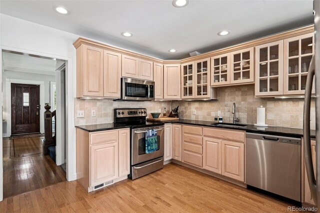 kitchen with appliances with stainless steel finishes, a sink, light brown cabinetry, glass insert cabinets, and light wood-style flooring