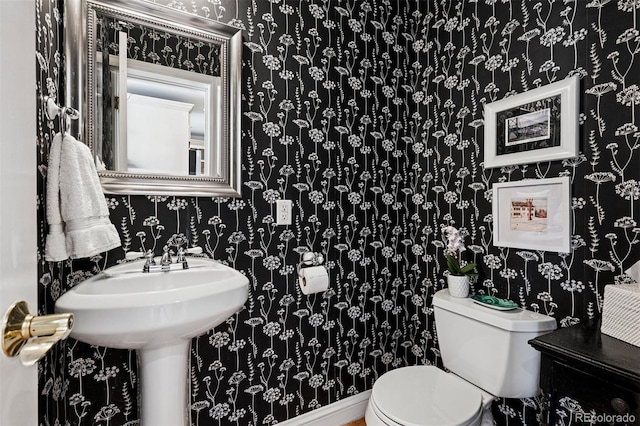 half bath featuring wallpapered walls and toilet