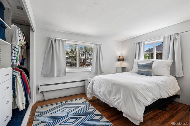 bedroom featuring a baseboard heating unit, multiple windows, and wood finished floors