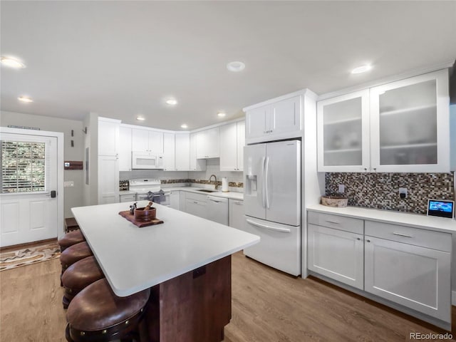 kitchen featuring sink, white cabinetry, light hardwood / wood-style flooring, a kitchen breakfast bar, and white appliances