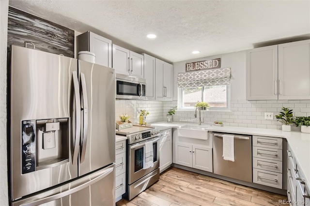 kitchen featuring white cabinets, light wood-style flooring, stainless steel appliances, light countertops, and a sink