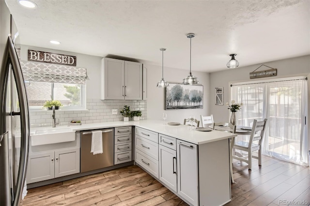 kitchen featuring appliances with stainless steel finishes, a peninsula, hanging light fixtures, light countertops, and a sink