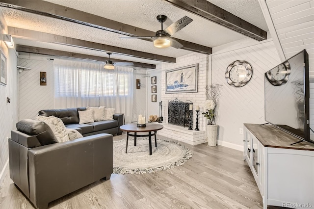 living area with light wood-style floors, a fireplace, a textured ceiling, and beamed ceiling