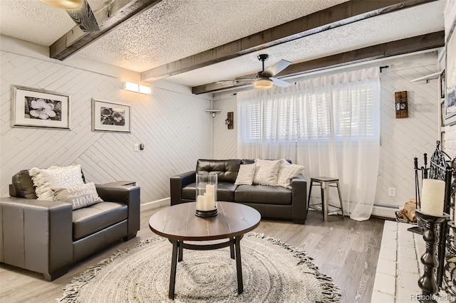 living room featuring light wood finished floors, baseboards, a textured ceiling, and beamed ceiling