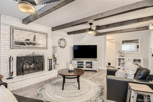 living area with a textured ceiling, a fireplace, a ceiling fan, light wood finished floors, and beamed ceiling