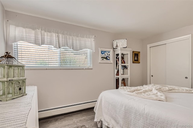 bedroom featuring a baseboard heating unit, a closet, and wood finished floors