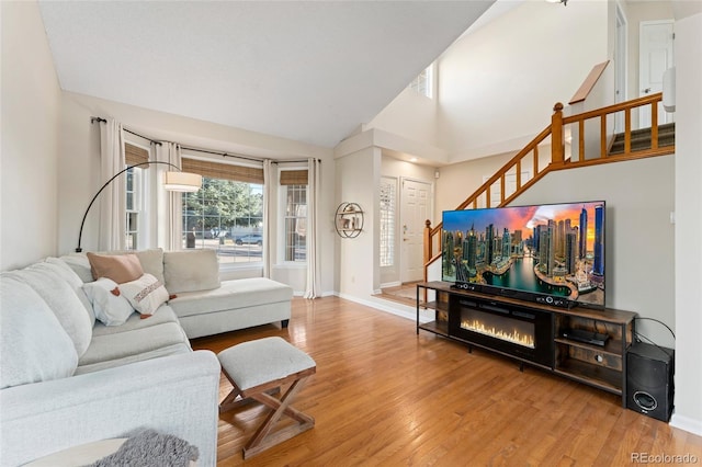 living area with lofted ceiling, wood finished floors, baseboards, stairway, and a glass covered fireplace