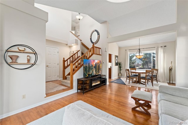 living room with visible vents, baseboards, wood finished floors, stairs, and vaulted ceiling