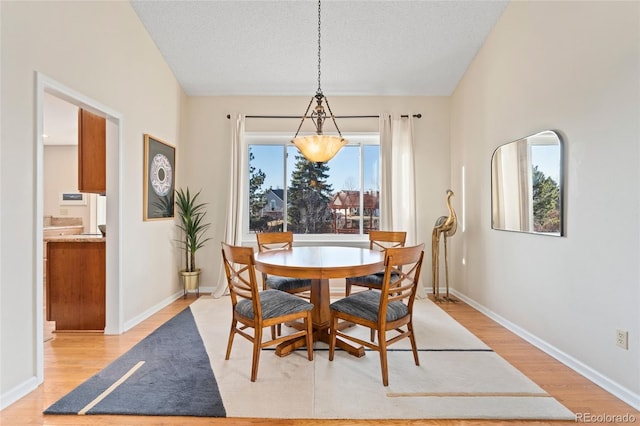 dining space with light wood-style floors, a textured ceiling, and baseboards