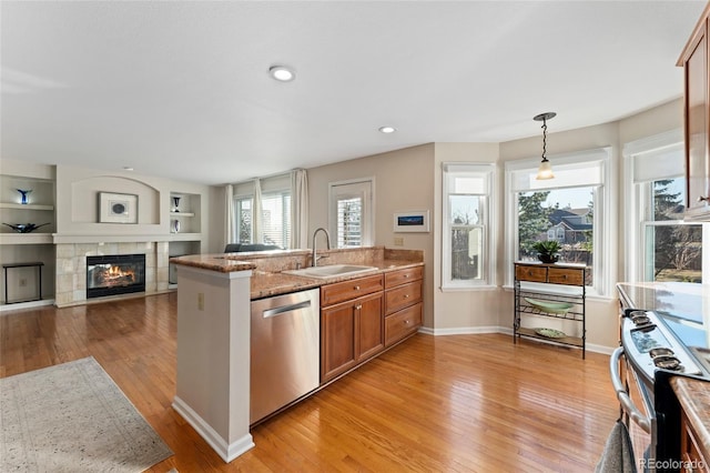 kitchen featuring brown cabinetry, a peninsula, stainless steel appliances, a fireplace, and a sink