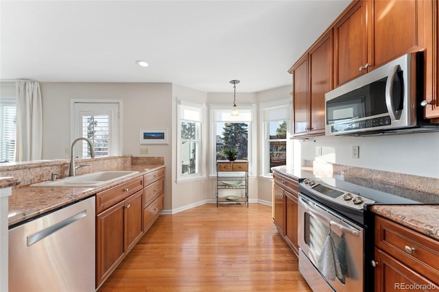 kitchen featuring brown cabinetry, decorative light fixtures, stainless steel appliances, light wood-style floors, and a sink