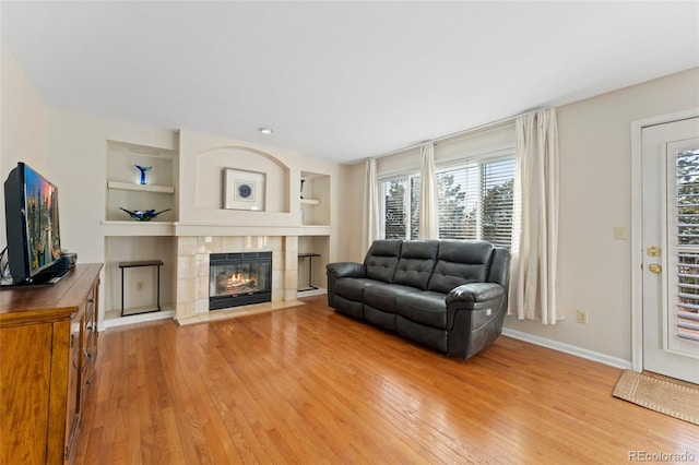 living room featuring light wood finished floors, built in shelves, baseboards, and a tiled fireplace