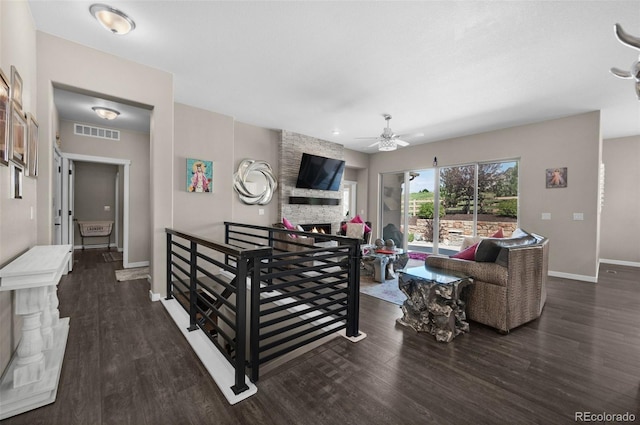 living room featuring visible vents, wood finished floors, baseboards, a stone fireplace, and a ceiling fan