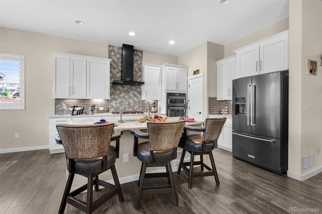 kitchen with an island with sink, white cabinetry, wall chimney range hood, a kitchen breakfast bar, and appliances with stainless steel finishes