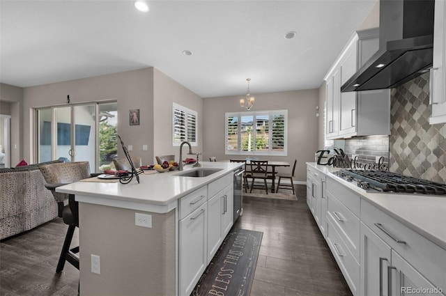 kitchen featuring appliances with stainless steel finishes, decorative light fixtures, a kitchen island with sink, sink, and wall chimney range hood