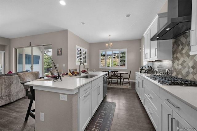 kitchen with appliances with stainless steel finishes, a sink, wall chimney exhaust hood, and dark wood finished floors