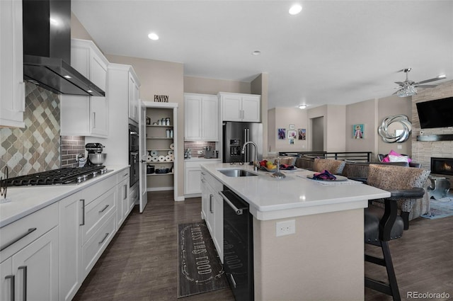 kitchen with wall chimney range hood, dark wood finished floors, a sink, and open floor plan