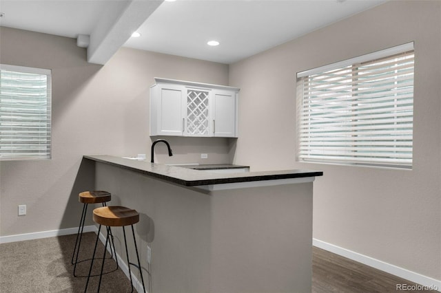 kitchen featuring a kitchen bar, baseboards, white cabinets, a peninsula, and recessed lighting