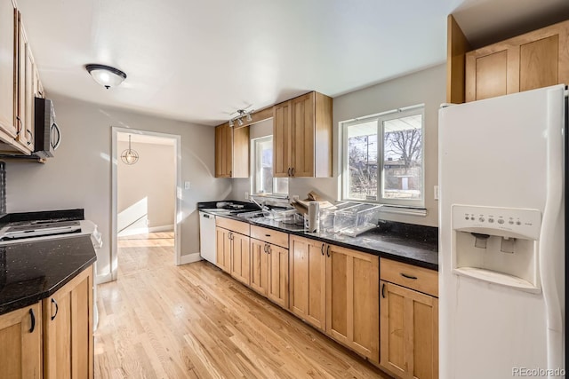 kitchen with dark stone countertops, sink, light hardwood / wood-style floors, and white appliances