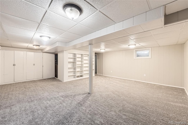 basement with a paneled ceiling, wooden walls, and carpet floors