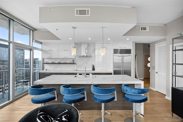 kitchen featuring light wood-type flooring, stainless steel built in fridge, backsplash, light stone counters, and white cabinets