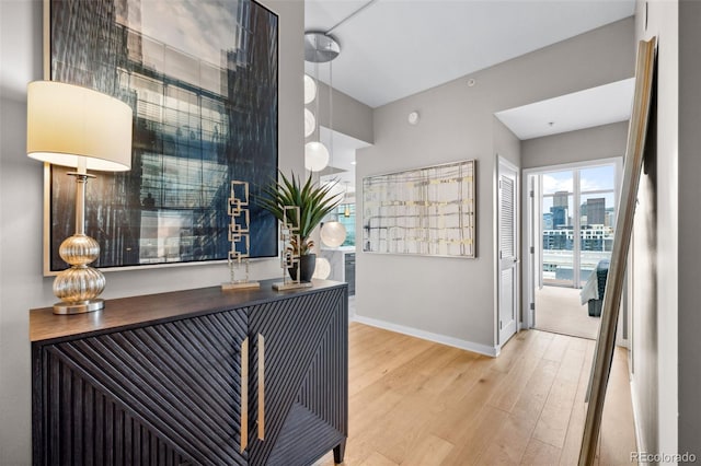 hallway featuring a view of city, light wood-style flooring, and baseboards