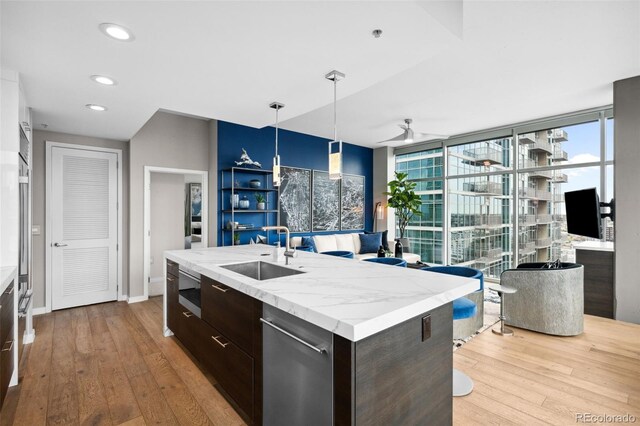 kitchen featuring a kitchen island with sink, a sink, light countertops, hanging light fixtures, and light wood finished floors