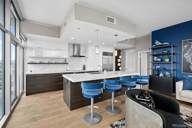 kitchen with dark brown cabinetry, open shelves, white cabinetry, wall chimney exhaust hood, and stainless steel built in refrigerator