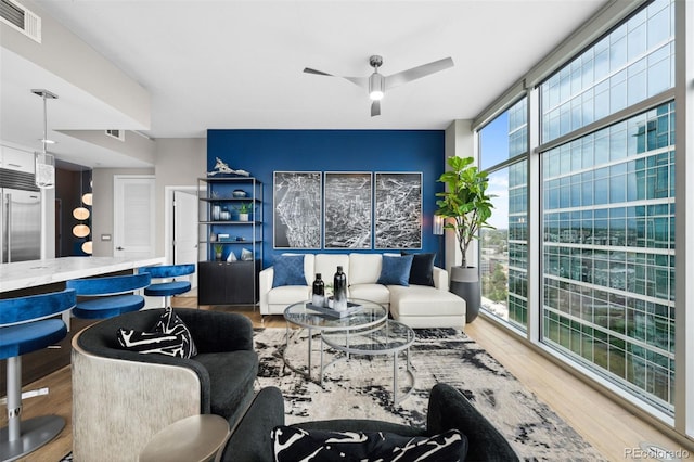 living area with a ceiling fan, visible vents, a wall of windows, and wood finished floors