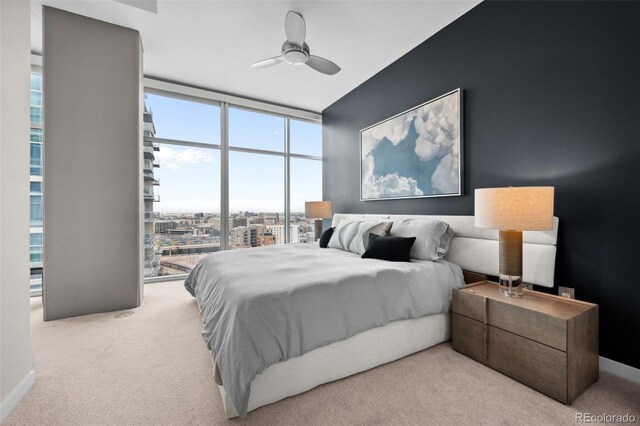 bedroom featuring baseboards, light colored carpet, ceiling fan, a view of city, and expansive windows