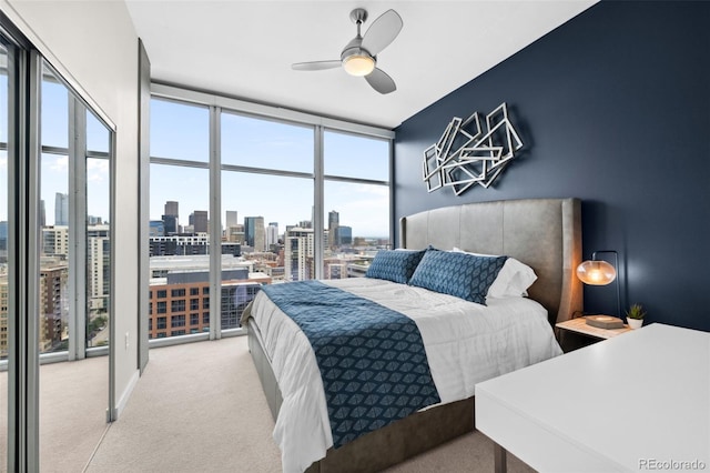 bedroom featuring a view of city, ceiling fan, expansive windows, and light carpet