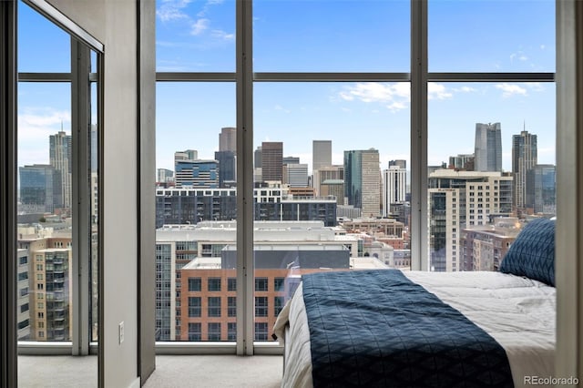 bedroom featuring a wall of windows, light colored carpet, a city view, and multiple windows