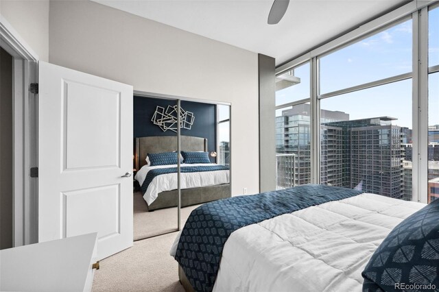 carpeted bedroom featuring a view of city, a wall of windows, and a ceiling fan