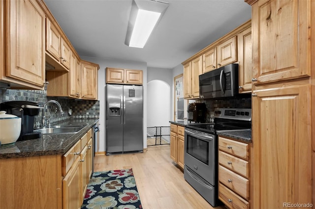 kitchen featuring sink, appliances with stainless steel finishes, tasteful backsplash, dark stone counters, and light hardwood / wood-style flooring