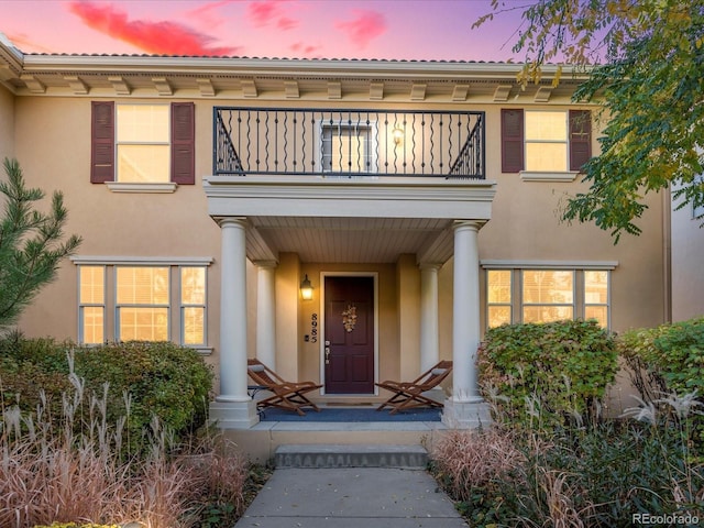 exterior entry at dusk featuring a balcony, covered porch, and stucco siding